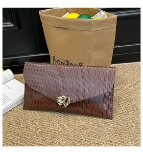 Détail d'une pochette enveloppe marron avec texture plissée et boucle en métal doré