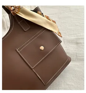 Detail of dark brown leather bucket bag with white contrast stitching and silk scarf
