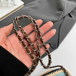 Detail van de gevlochten metalen kettingriem met bruin leer op de strooien handtas