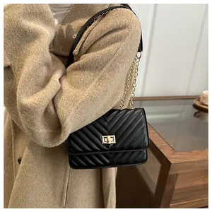Détail du sac bandoulière en cuir noir matelassé avec chaîne dorée sur un manteau