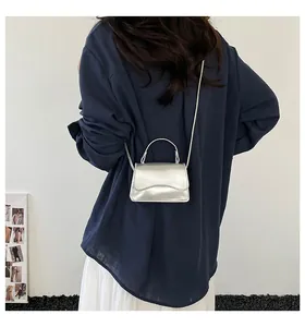 Sac à bandoulière argenté effet miroir porté par un mannequin en jupe blanche longue