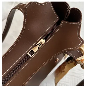 Macro detail of brown leather bucket bag with white stitching, gold zipper, and silk scarf