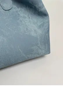 Close-up of blue washed denim fabric texture and soft structure on a tote shoulder bag