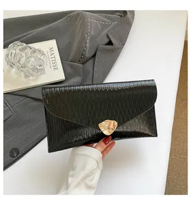 Détail de pochette enveloppe noire à texture ondulée et boucle dorée sur un blazer