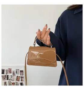 Détail d'un mini sac à main marron brillant avec rabat ondulé porté par un mannequin