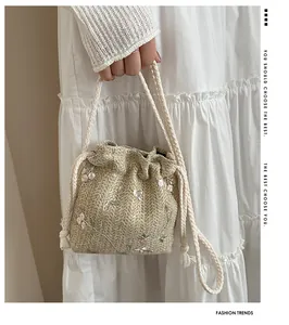 Detail of woven straw bucket bag with floral embroidery and white cotton drawstring handles