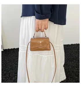 Détail du mini sac en cuir verni caramel avec bord à rabat ondulé et poignée supérieure