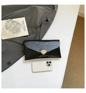 Détail d'une pochette enveloppe noire brillante avec texture ondulée et boucle en métal doré