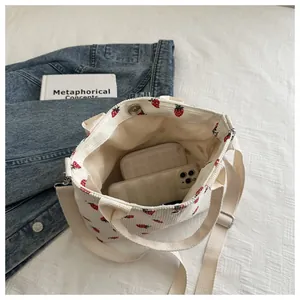 Detail of strawberry print corduroy bag showing adjustable strap and magnetic closure