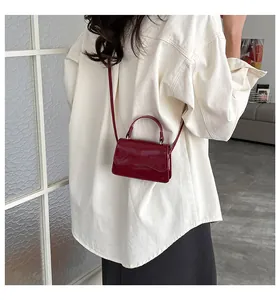 Détail du mini sac en cuir verni rouge foncé avec rabat ondulé et fine bandoulière