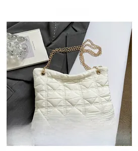 Detail of white quilted cloud bag with gold chain over a grey blazer and art book