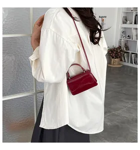 Détail d'un mini sac à main en cuir verni bordeaux brillant avec une poignée ronde