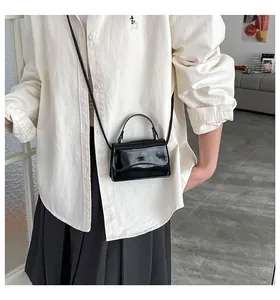 Sac à bandoulière mini en cuir verni noir porté avec rabat ondulé et finition brillante