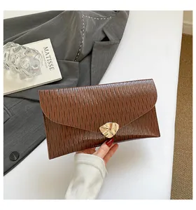 Détail d'une pochette enveloppe marron foncé avec fermoir en métal doré et texture