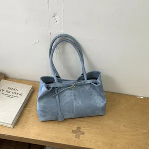 Close-up of matte blue leather tote bag with gold buckle detail on wooden bench