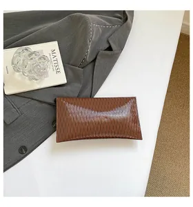 Détail d'une pochette en cuir verni marron foncé avec texture ondulée sur fond de costume