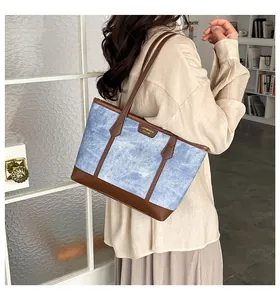 Detail showing the light blue denim fabric with brown leather trim on the tote bag