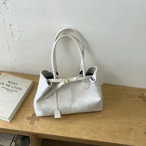 Detail view of cream tote bag with gold buckle and leather tag on a wooden table