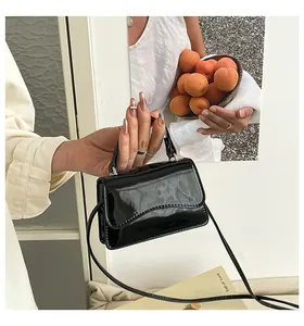 Détail d'un petit sac en cuir verni noir brillant avec rabat ondulé et texture miroir