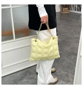 Detail of light yellow quilted puffy bag with golden chain strap held by a person