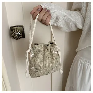 Detail of embroidered pink flowers on a beige woven bucket bag with rope handles