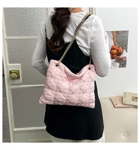 Pink quilted puff shoulder bag with golden chain strap worn by a model in a cozy room