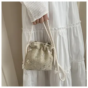 Detail der Stroh-Eimertasche mit pastellfarbenen Blumenstickereien und Seilgriff