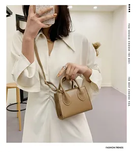 Beige mini crossbody bag with leather texture and top handle shown on a white dress