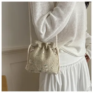 Detail of woven straw bucket bag with delicate floral embroidery and drawstring closure