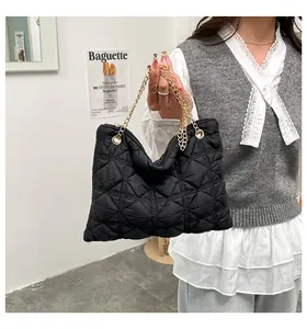 Detail of black quilted puffer bag with gold chain strap held by model against white wall