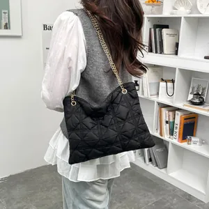 Chic black quilted puff tote bag with gold chain strap shown on a model's shoulder