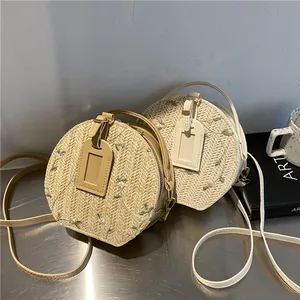 Fashionable round straw shoulder bag with floral embroidery and adjustable leather strap