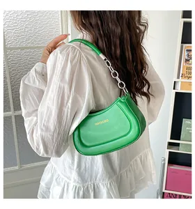 Detail der grünen sichelförmigen Schultertasche mit Silberkette und goldenem Logo-Schriftzug