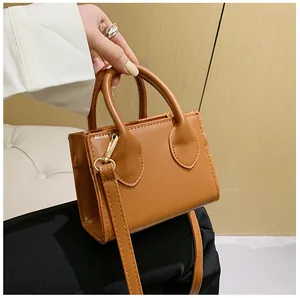 Close-up of tan leather mini square handbag with round handles and gold metal hardware