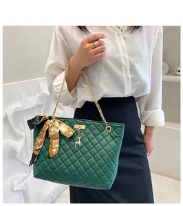 Model wearing dark green quilted tote bag with gold chain strap and decorative scarf