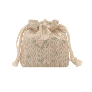 Minimalist woven straw bucket bag with floral embroidery and tassel drawstring closure