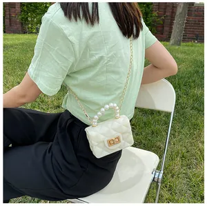 Outdoor shot of a mini white quilted bag with pearl handle and gold chain strap