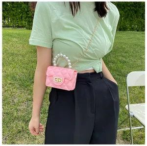 Pink mini jelly bag with pearl handle and gold chain strap shown against a grass field