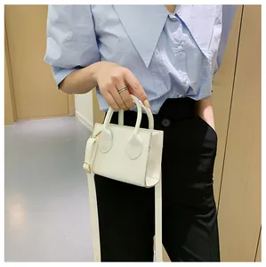 Close-up of minimalist white mini handbag with double handles and gold metal buckles