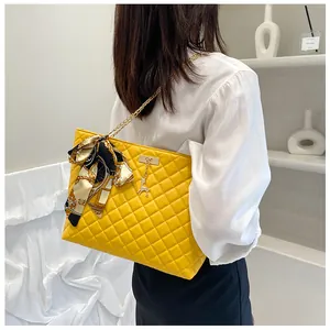 Detail of yellow quilted tote bag featuring gold chain and decorative silk scarf