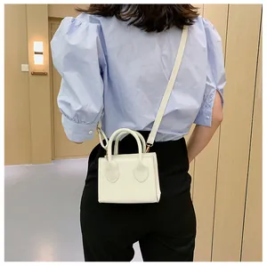 Chic cream-white mini rectangular crossbody bag held by a model in a puff-sleeve shirt