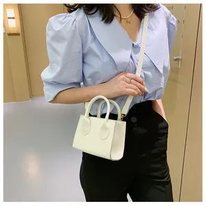 Close-up of white mini square crossbody bag with dual ring handles and long strap