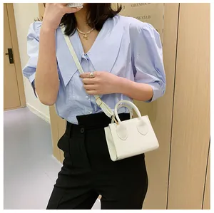 Chic white mini square handbag with dual handles worn over a blue shirt