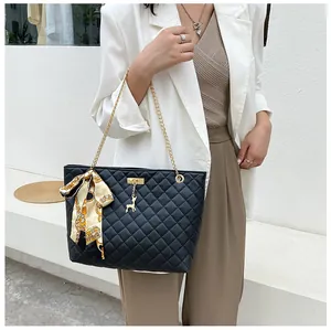 Quilted black shoulder bag with gold chain and silk scarf shown on model in white blazer