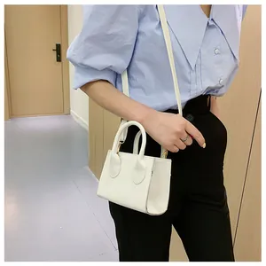 Detail view of a white mini handbag with gold hardware worn as a crossbody by a model