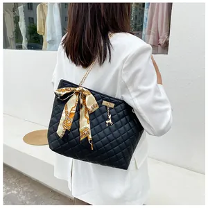 Detail of black quilted tote bag with gold chain strap and decorative silk scarf