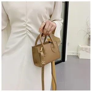 Detail of a camel mini handbag with gold metal buckles and a white dress background