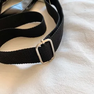 Detail of a thick black canvas shoulder strap with a polished silver metal buckle
