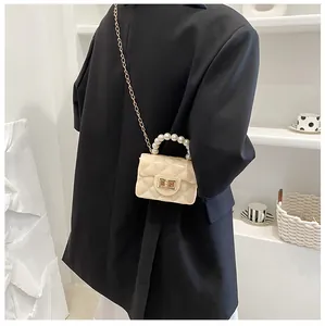 Chic quilted mini crossbody bag with pearl handle and gold chain worn on black blazer