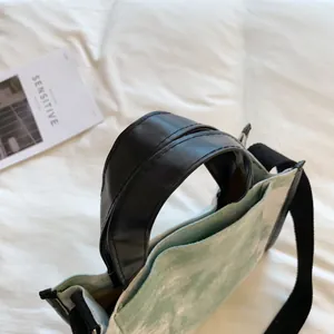 Detail of tie-dye canvas handbag with black leather handles and shoulder strap